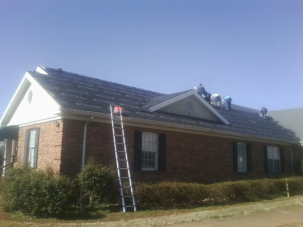 Crew tearing shingles off a brick ranch roof with a ladder set — Emergency Roof Repair work by our crew in Dellroy