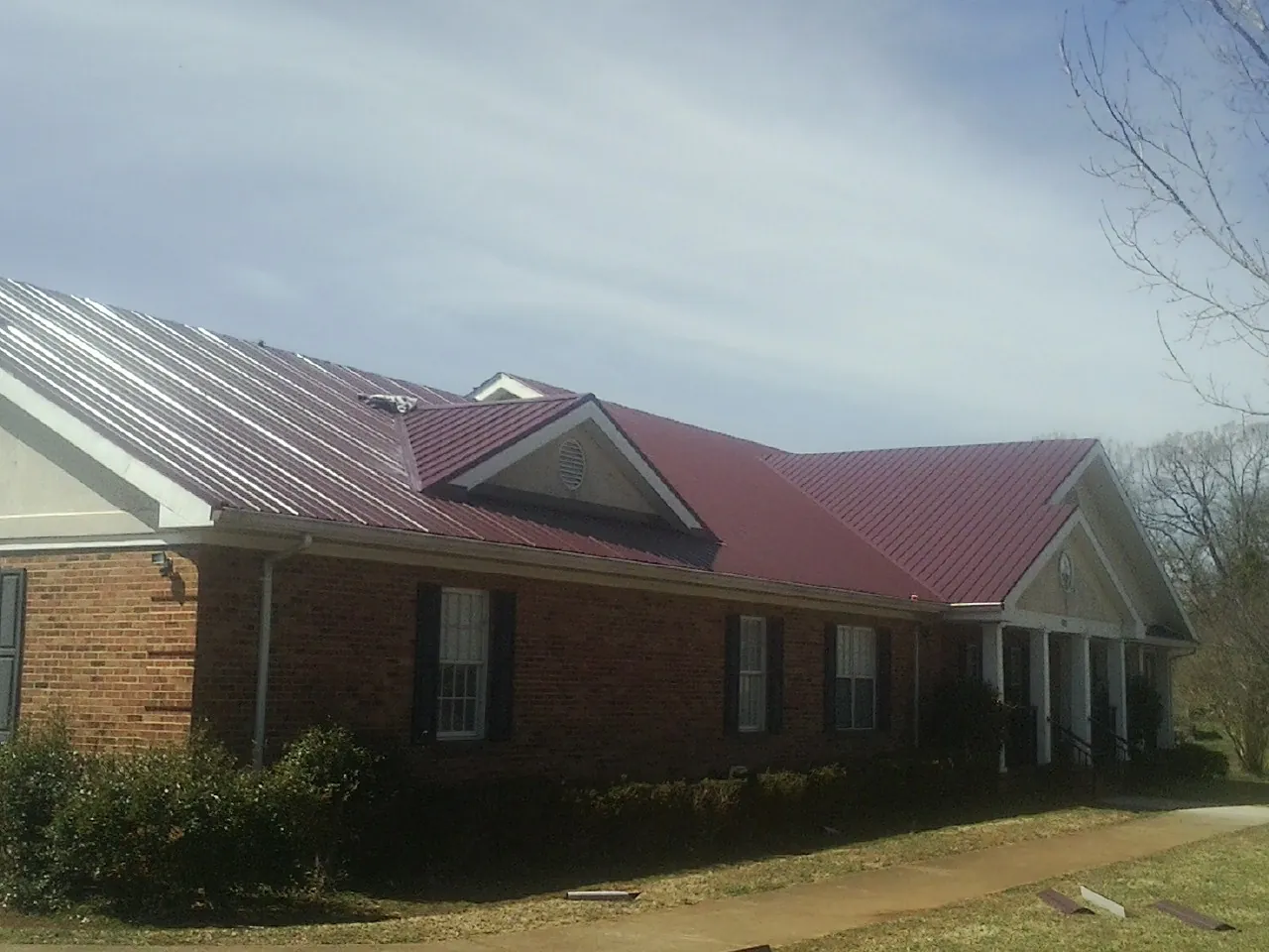 Red metal roof with gabled entries on a long brick building, from a Hail Damage Roof Repair job in Dellroy