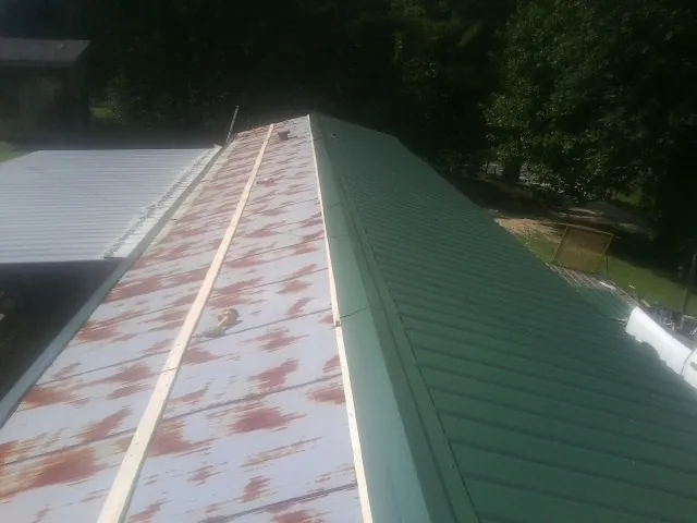 Old rusted panels beside newly installed green metal roofing — Wind Damage Roof Repair by Roofing Brothers in Dellroy