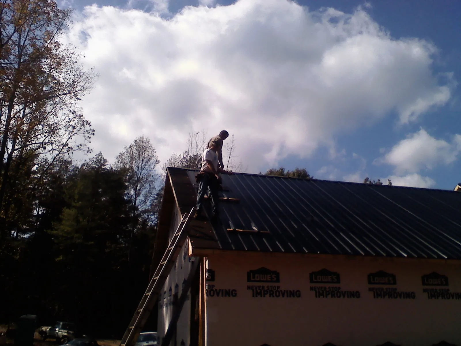 Roofer fastening dark metal panels high against a cloudy sky, from a Roof Inspection job in Dellroy