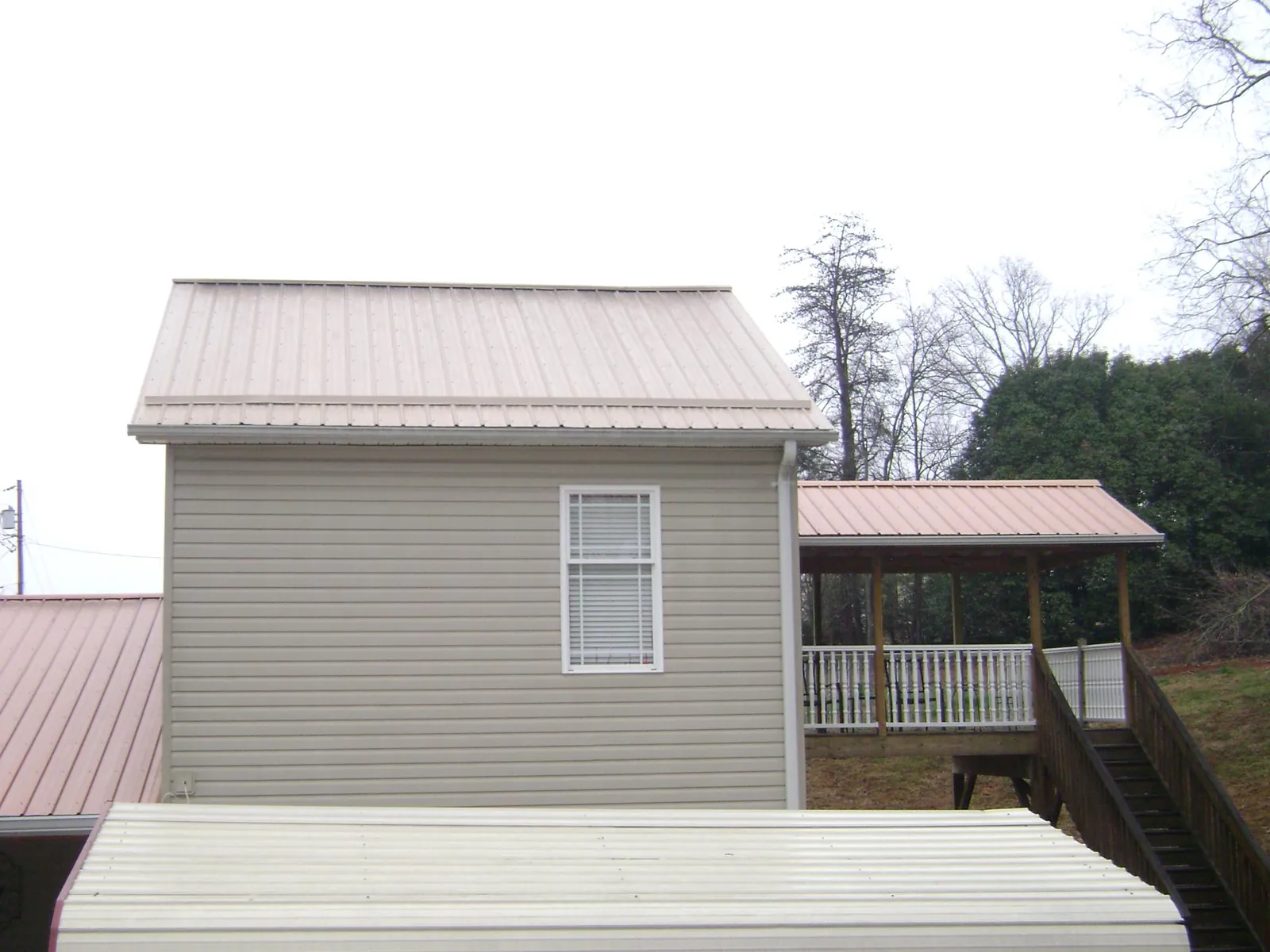 Tan metal roofs on a two story addition and attached porch, from a Roof Replacement job in Dellroy
